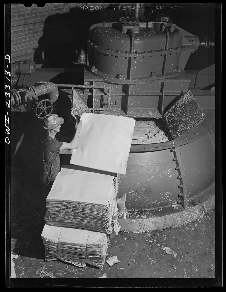 Archival photograph of paper sheets being fed into a vortex beater at a paper mill in 1943